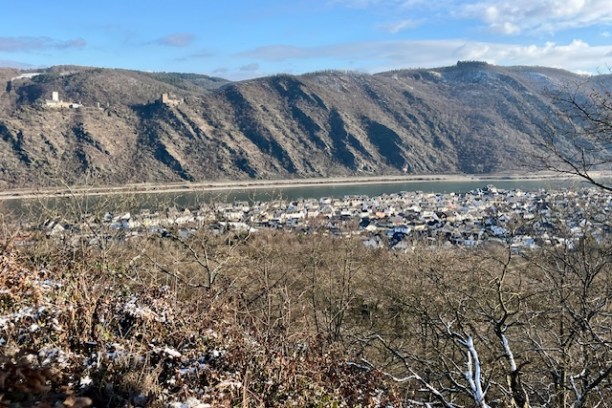 River with hillside town, distant mountains, and clear sky on a sunny day.